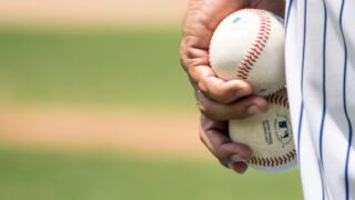 man holding two white baseballs